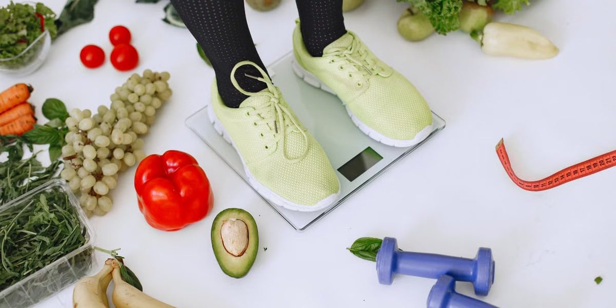 Person standing on scales surrounded by fresh produce and fitness equipment symbolizing a balanced lifestyle.