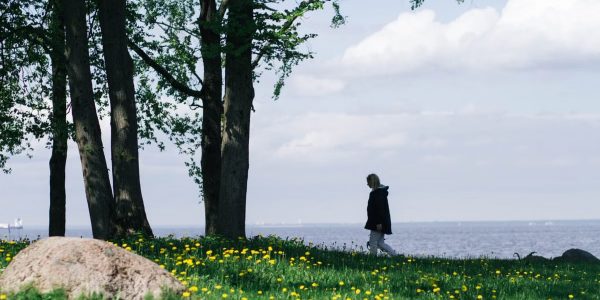 A woman walks along a grassy field by a serene lake under a clear spring sky.