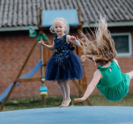 Two girls enjoy jumping on a trampoline outside. Fun and laughter in a playful setting.
