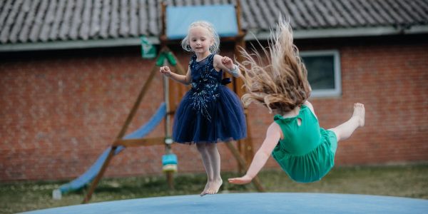 Two girls enjoy jumping on a trampoline outside. Fun and laughter in a playful setting.
